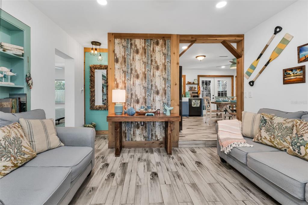 A living room features two gray sofas, wood-look tile flooring, and a rustic wood accent wall — 115 WINSON AVENUE, ENGLEWOOD, FL