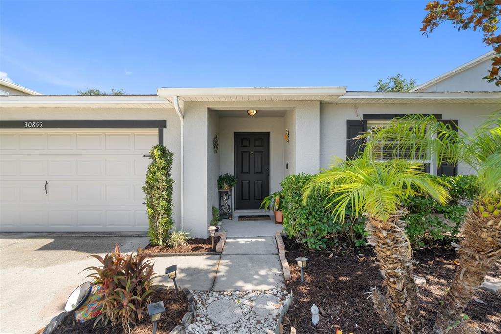 The exterior of a single-story house features a garage, a front entrance, and landscaping — 30855 TEMPLE STAND AVENUE, WESLEY CHAPEL, FL