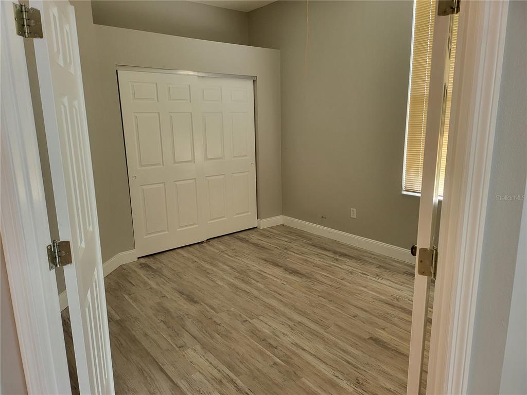 An empty bedroom features light wood-look flooring, gray walls, and white sliding closet doors — 502 CATALINA ISLES CIRCLE, VENICE, FL
