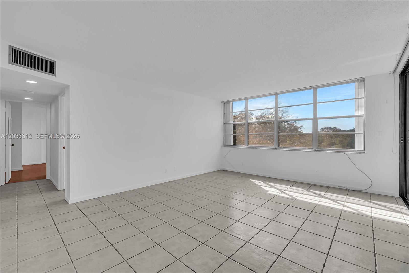 An empty room features light-colored tile flooring, white walls, and a large window — 2781 Taft St # 303, Hollywood FL 33020, HOLLYWOOD, FL