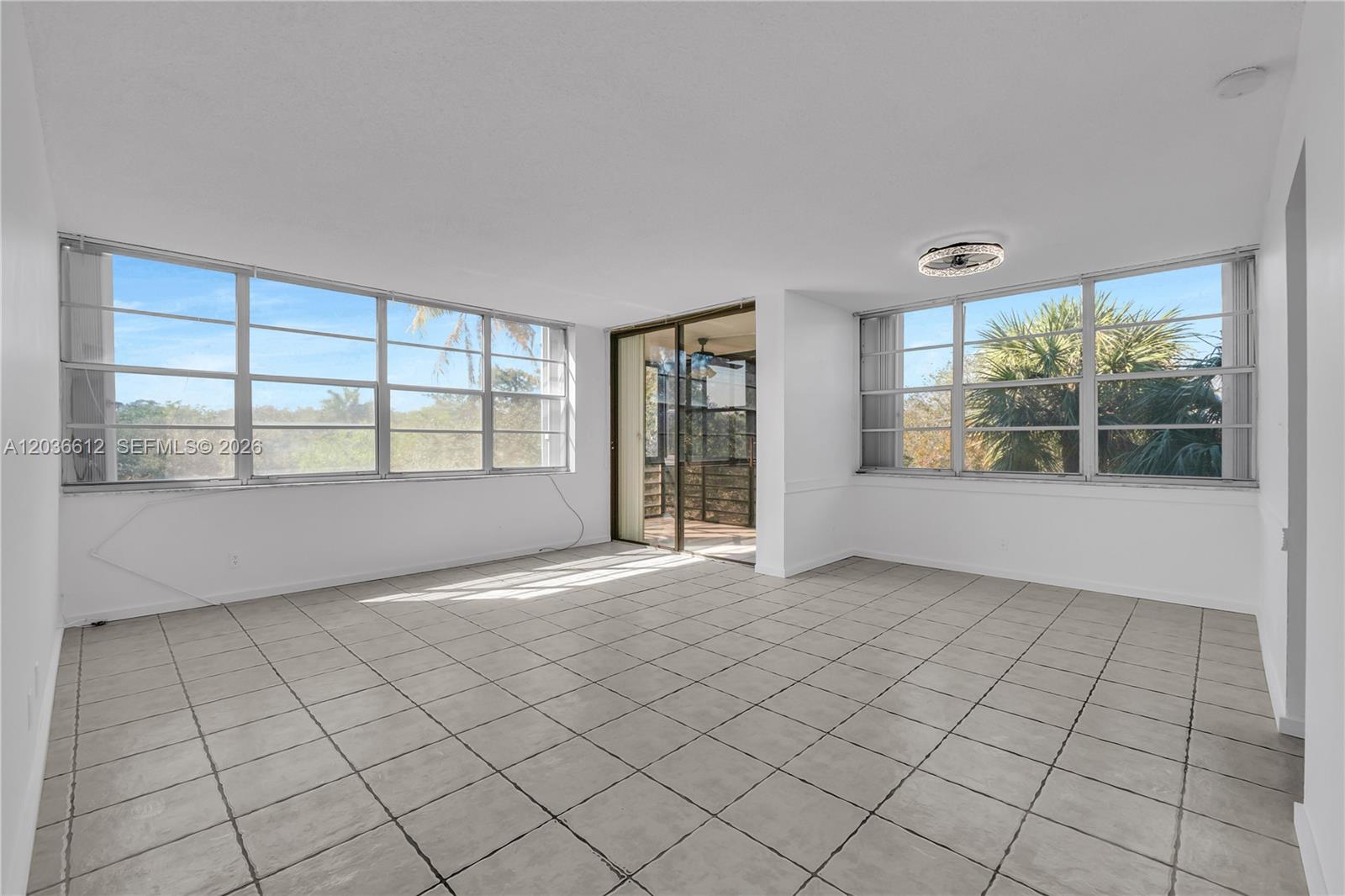 An empty room features light-colored tile flooring, white walls, large windows, and a sliding glass door — 2781 Taft St # 303, Hollywood FL 33020, HOLLYWOOD, FL
