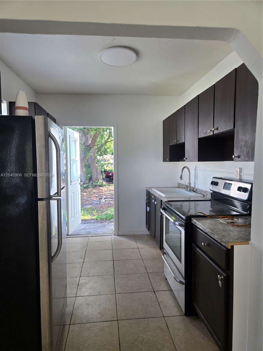 A galley kitchen features dark cabinets, stainless steel appliances, tile flooring, and an exterior door — 5223 SW 25th St # 0, West Park FL 33023, WEST PARK, FL