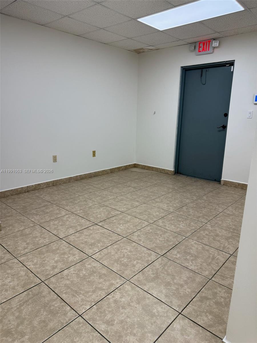 An empty room features white walls, tan tiled flooring, and a gray exit door — 6995 NW 82nd Ave # 45, Medley FL 33166, MEDLEY, FL