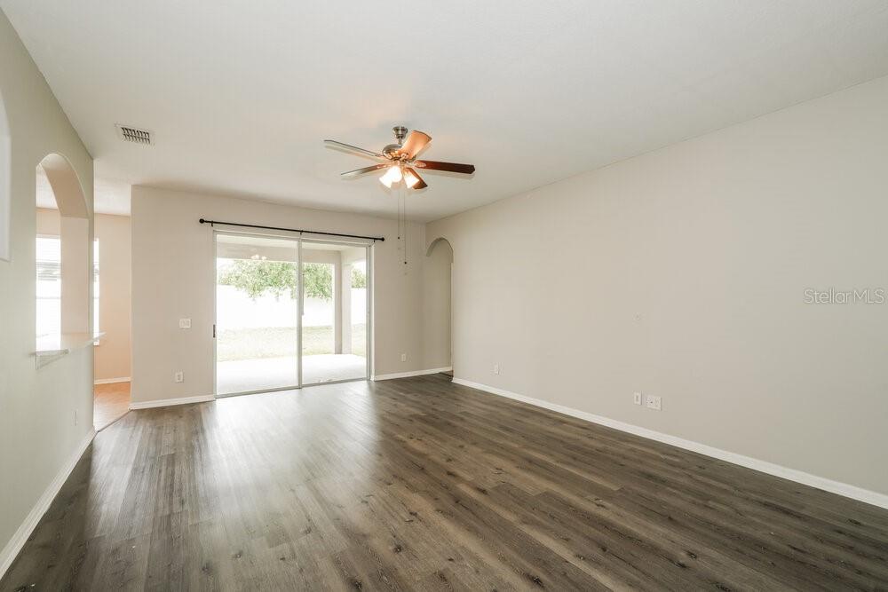 An empty living room features wood-look flooring, a ceiling fan, and sliding glass patio doors — 7726 BULLS HEAD DRIVE, WESLEY CHAPEL, FL