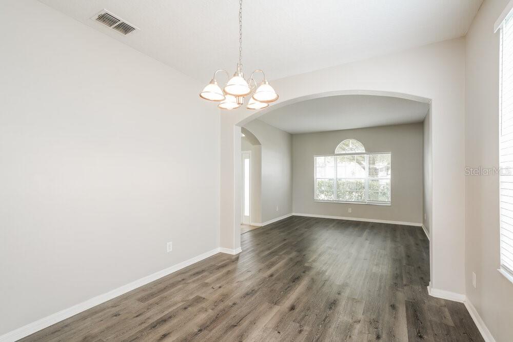 An empty dining area with a chandelier leads into a living room with wood flooring — 7726 BULLS HEAD DRIVE, WESLEY CHAPEL, FL