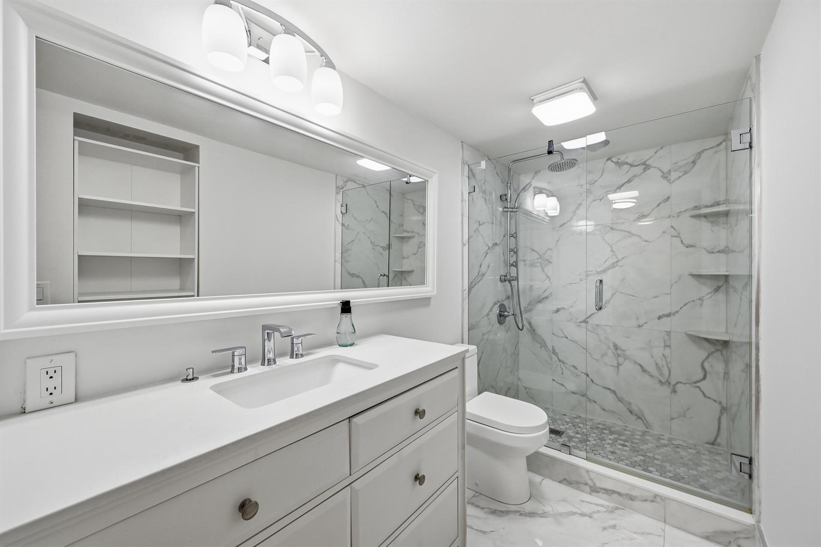 A modern bathroom features a white vanity, a large mirror, and a glass-enclosed marble shower — 2006 Granada Drive # M3, Coconut Creek FL 33066, COCONUT CREEK, FL
