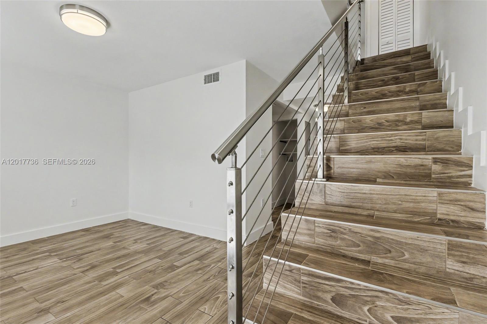 A room features wood-look tile flooring and a staircase with a modern metal cable railing — 122 SW 56th Ave, Miami FL 33134, MIAMI, FL