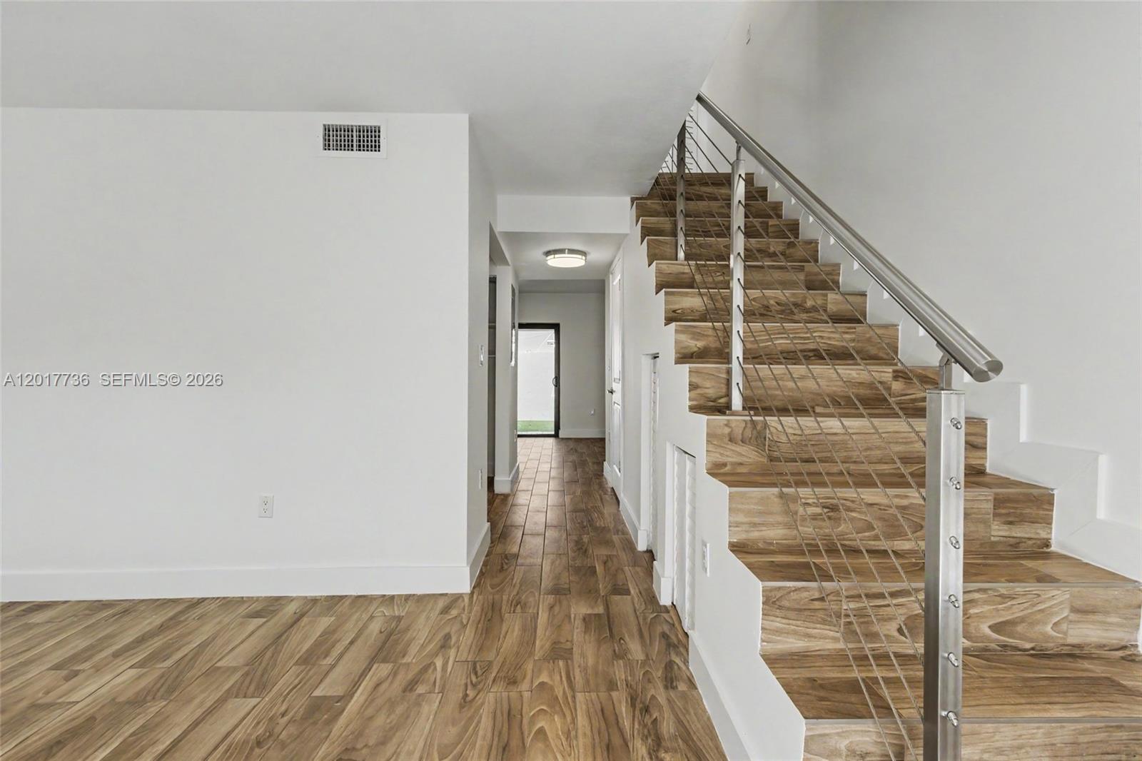 A staircase with wood-look treads and a metal railing sits beside a hallway with tile flooring — 122 SW 56th Ave, Miami FL 33134, MIAMI, FL