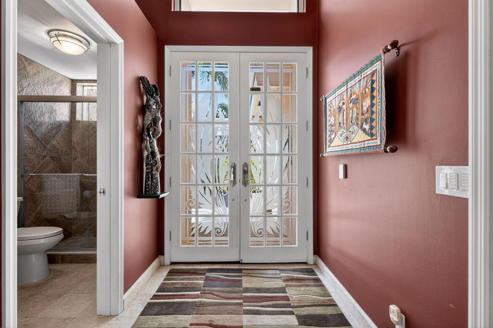 An entryway with red walls, a patterned rug, double glass doors, and an adjacent bathroom — 402 Eagleton Cove Way, Palm Beach Gardens FL 33418, PALM BEACH GARDENS, FL