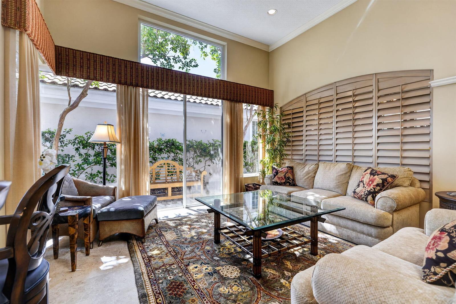 A living room features a glass coffee table, beige sofas, and large windows with shutters — 402 Eagleton Cove Way, Palm Beach Gardens FL 33418, PALM BEACH GARDENS, FL