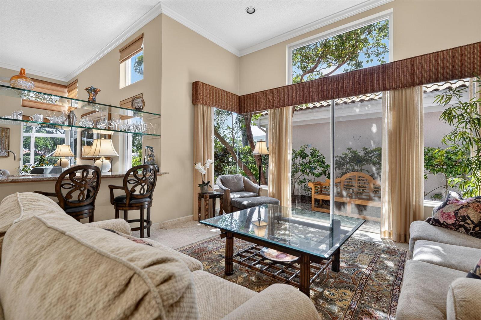 A living room with a bar area, glass coffee table, and large windows overlooking a patio — 402 Eagleton Cove Way, Palm Beach Gardens FL 33418, PALM BEACH GARDENS, FL