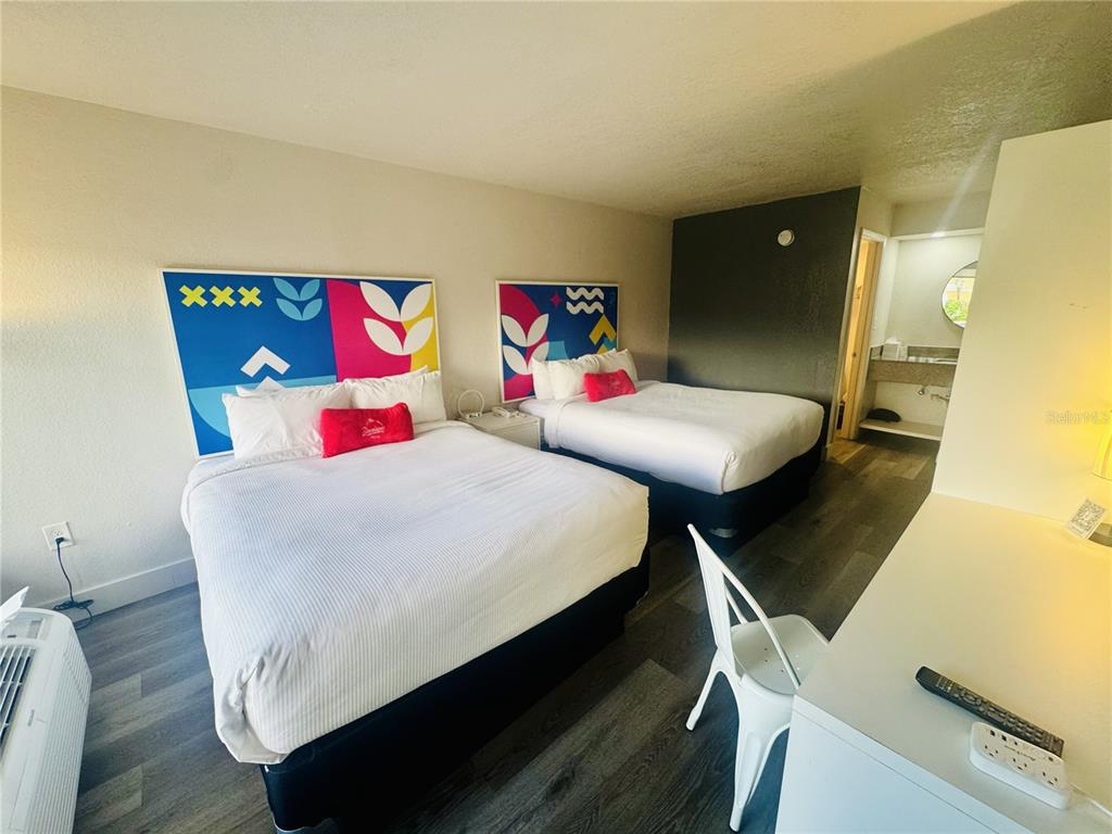 A hotel room features two beds with colorful headboards, wood-look flooring, and an attached bathroom — 2930 POLYNESIAN ISLE BOULEVARD UNIT 105, KISSIMMEE, FL
