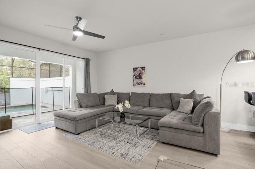 A living room features a large gray sectional sofa, a glass coffee table, and sliding doors opening to a pool — 17350 BLESSING DRIVE, CLERMONT, FL