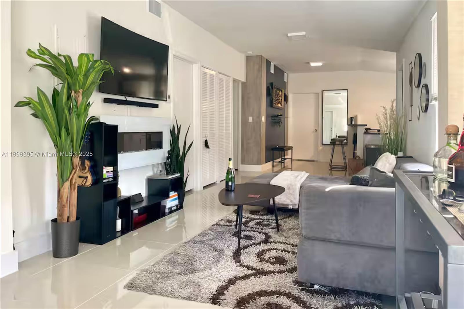 A modern living room features a fireplace, wall-mounted television, gray sectional sofa, and area rug — 3132 NW 43rd St, Miami FL 33142, MIAMI, FL