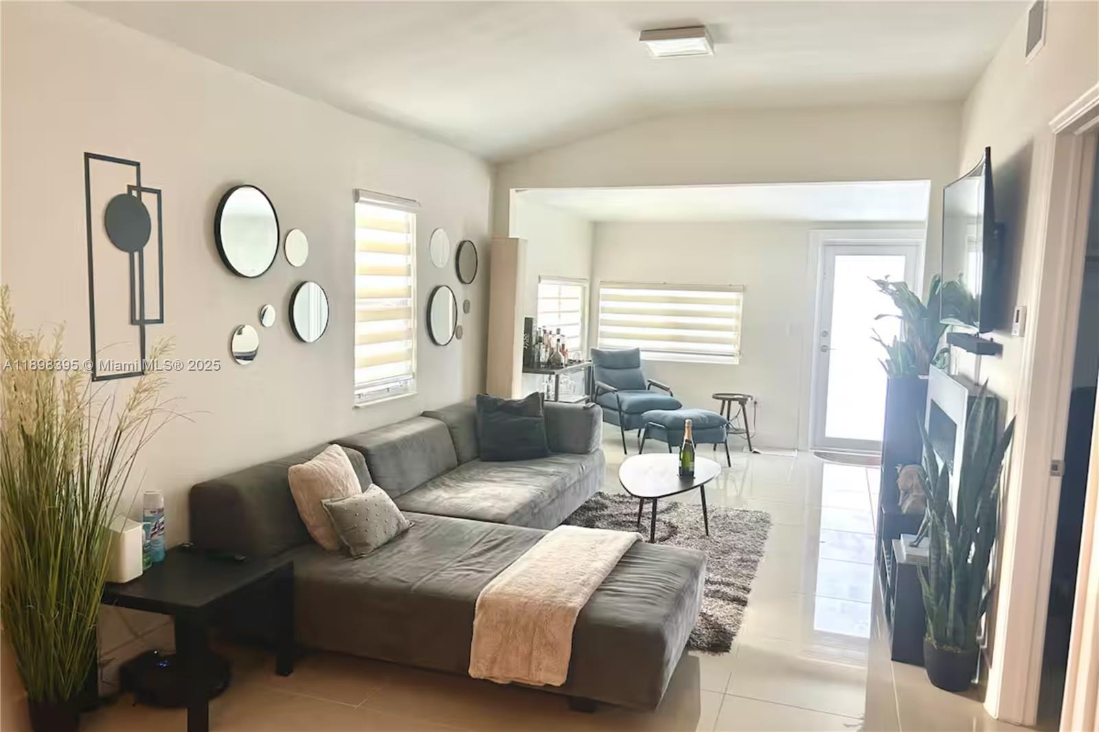 A living room features a grey sectional sofa, tiled floors, and a wall of mirrors — 3132 NW 43rd St, Miami FL 33142, MIAMI, FL