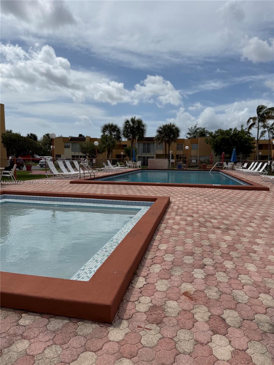 An outdoor swimming pool area features a smaller spa and a larger pool with pavers — 9320 W Flagler St # 201D, Miami FL 33174, MIAMI, FL