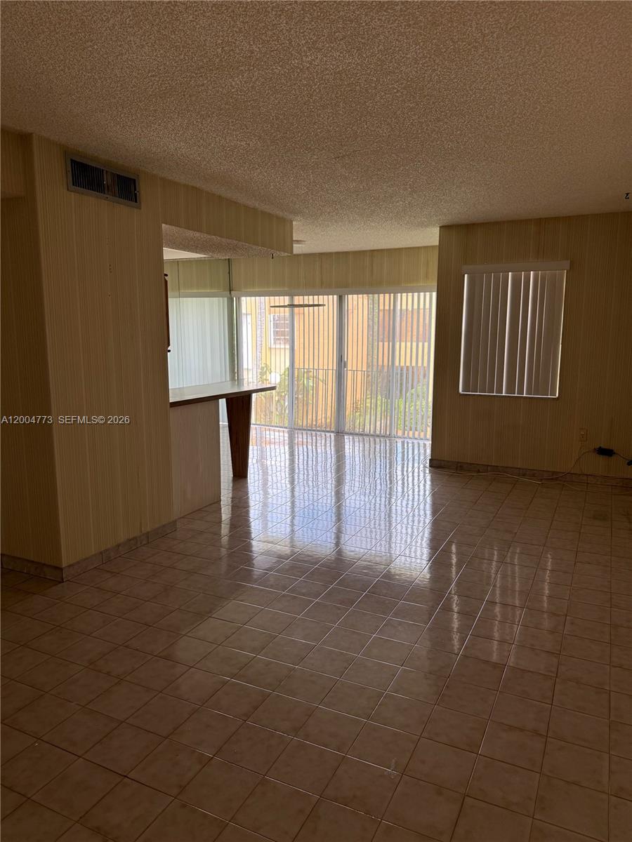 An empty room features beige tiled floors, vertical striped wallpaper, and a sliding glass door — 9320 W Flagler St # 201D, Miami FL 33174, MIAMI, FL