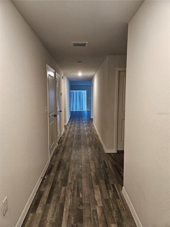 A long hallway with wood-look flooring leads to a room with vertical blinds — 901 NW 15TH PLACE, CAPE CORAL, FL