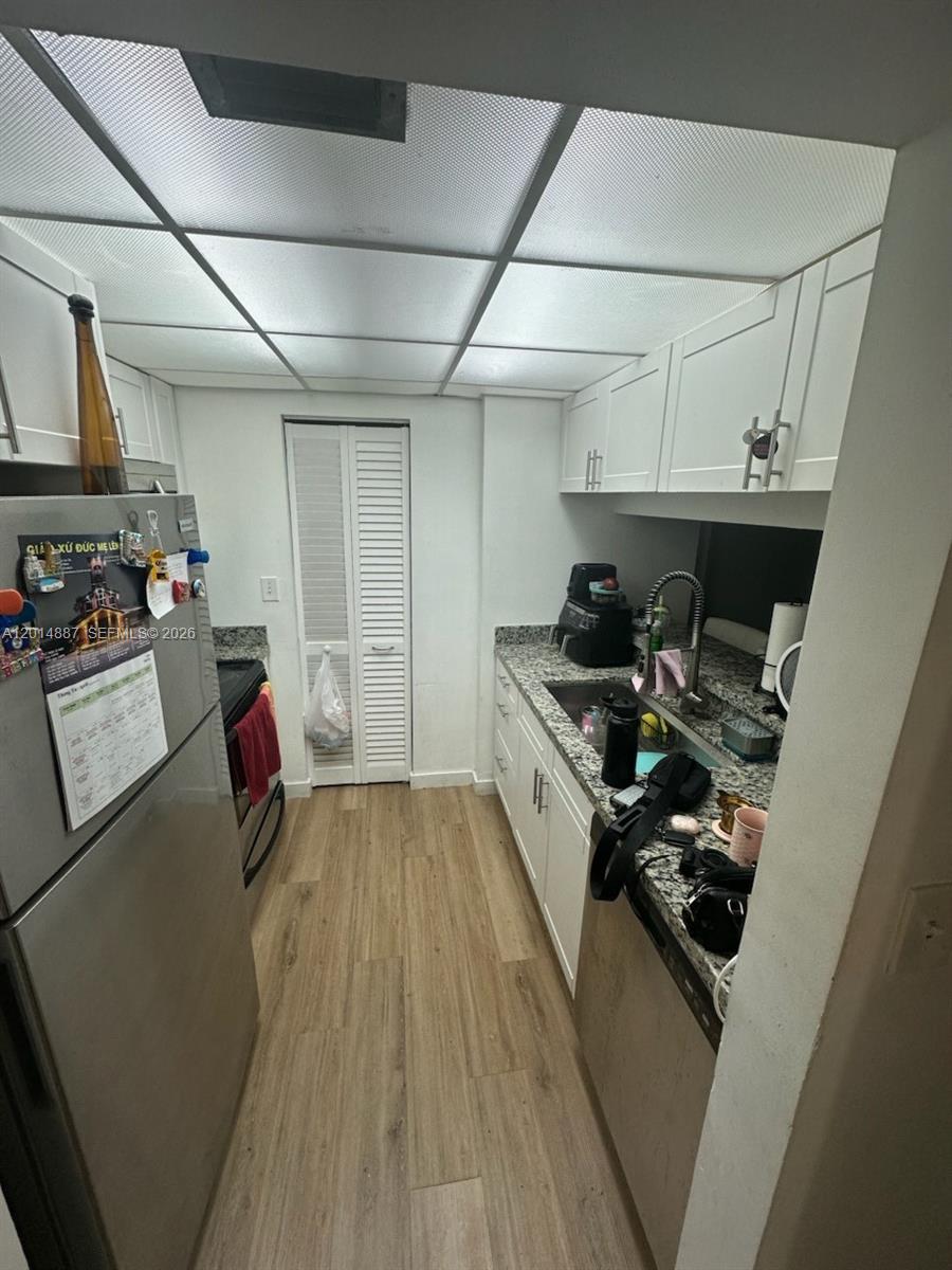 A galley-style kitchen features white cabinets, granite countertops, stainless steel appliances, and wood-look flooring — 800 N MIAMI AVE # 1210, Miami FL 33136, MIAMI, FL