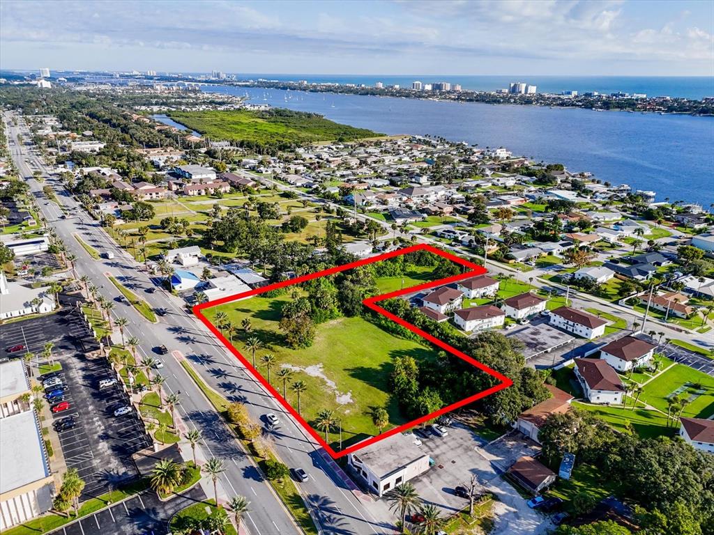 An aerial view shows a vacant, L-shaped grassy lot outlined in red near a waterfront — 1771 S RIDGEWOOD AVENUE, SOUTH DAYTONA, FL