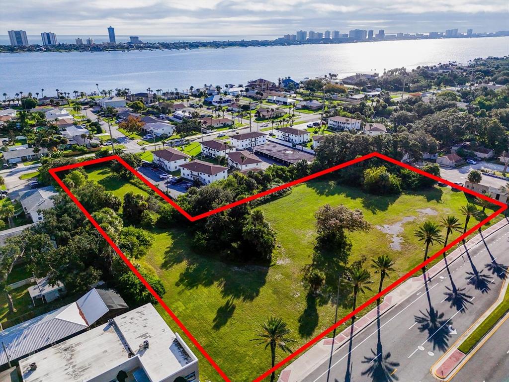 An aerial view shows a large, vacant grassy lot outlined in red near a waterfront — 1771 S RIDGEWOOD AVENUE, SOUTH DAYTONA, FL