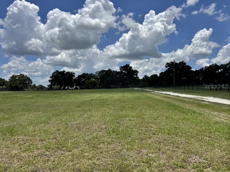 A grassy field with a dirt path and a wooden fence under a cloudy sky — NW 131 STREET, REDDICK, FL