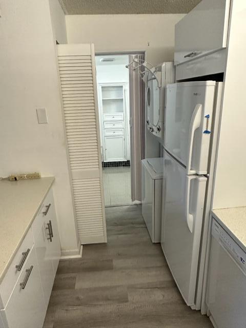 A kitchen features white cabinetry, a refrigerator, a stacked washer-dryer, and light wood-look flooring — 1106 Green Pine Boulevard # E1, West Palm Beach FL 33409, WEST PALM BEACH, FL