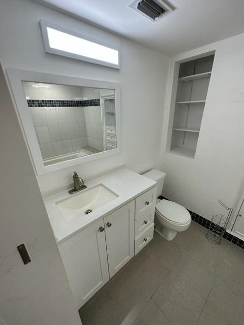 A bathroom featuring a white vanity, a rectangular mirror, a toilet, and built-in wall shelving — 1106 Green Pine Boulevard # E1, West Palm Beach FL 33409, WEST PALM BEACH, FL