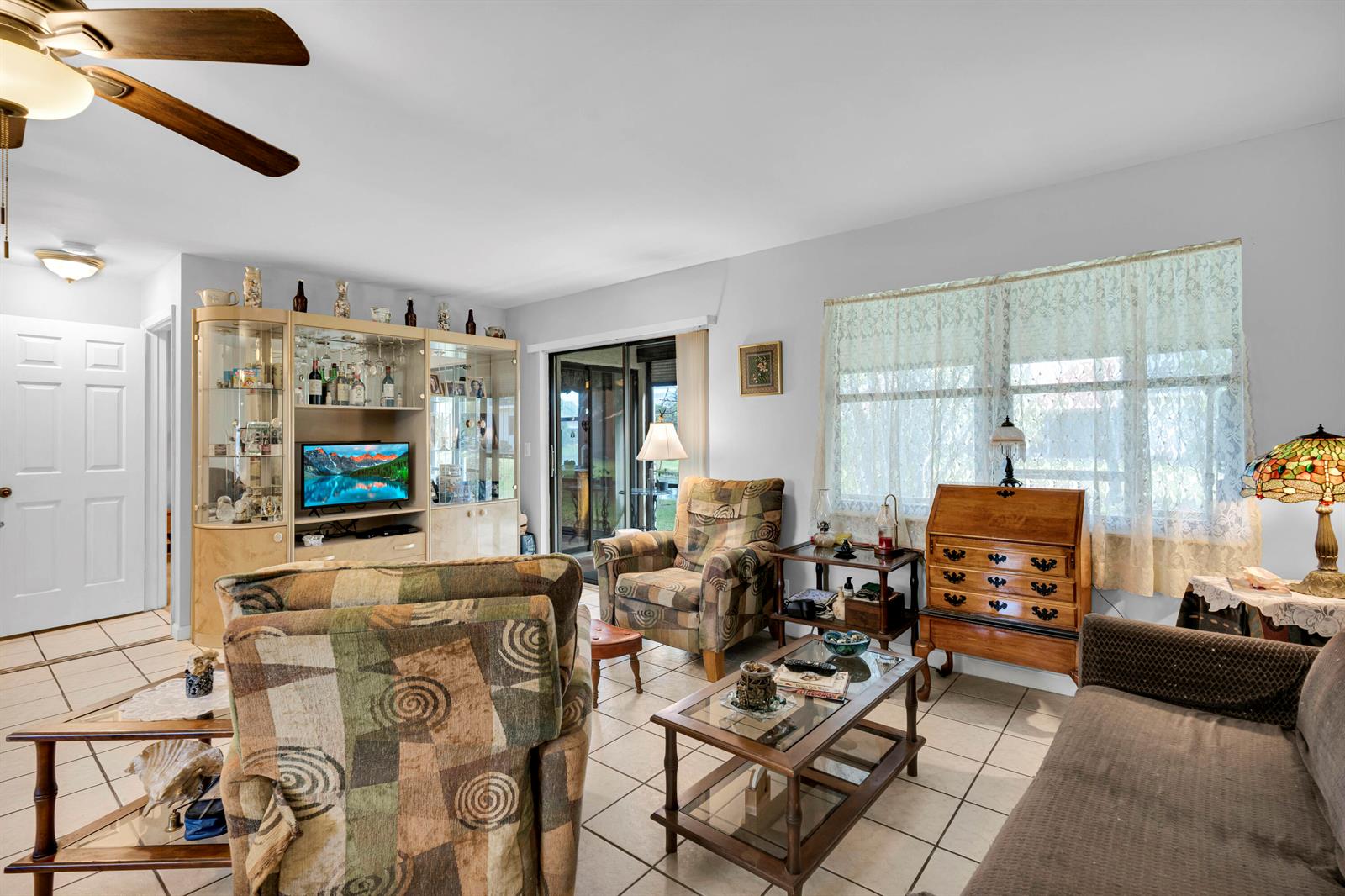 A living room features tile flooring, patterned armchairs, a glass coffee table, and a hutch — 3 Vía De Casas Sur # 102, Boynton Beach FL 33426, BOYNTON BEACH, FL