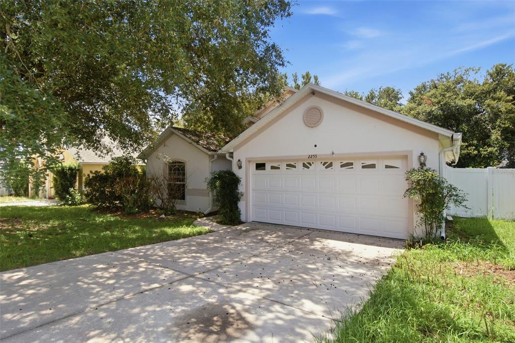 A single-story house with a white garage door, concrete driveway, and large shade trees — 2255 MERRY ROAD, TAVARES, FL