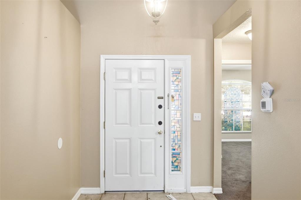 An entryway features a white front door with a decorative glass sidelight and tile flooring — 2255 MERRY ROAD, TAVARES, FL