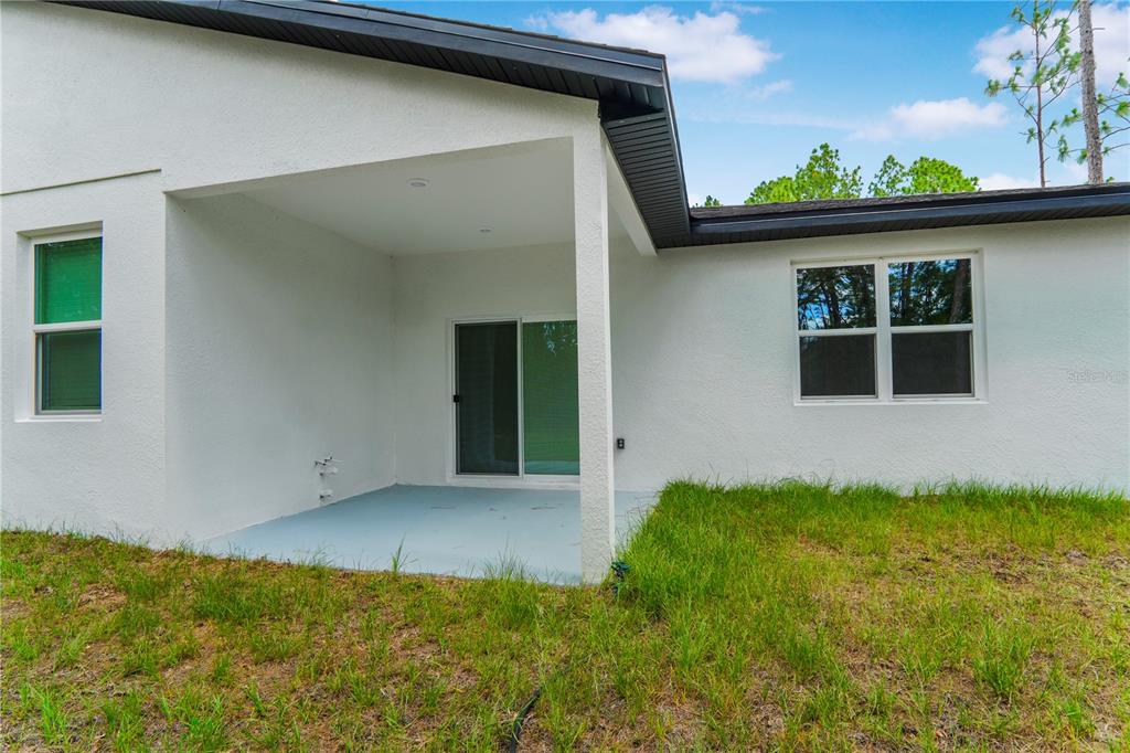 The exterior view shows a white stucco house with a covered patio and sliding glass doors — 1902 W ADELIA PLACE, CITRUS SPRINGS, FL