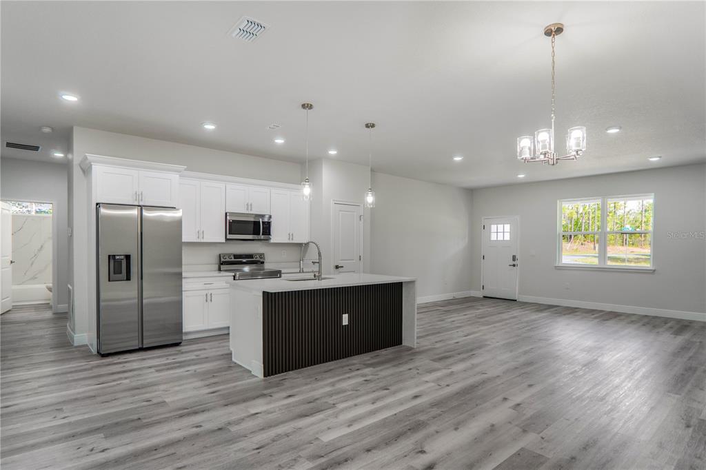 A modern open-concept kitchen and living area features white cabinetry, a slatted island, and flooring — 1902 W ADELIA PLACE, CITRUS SPRINGS, FL