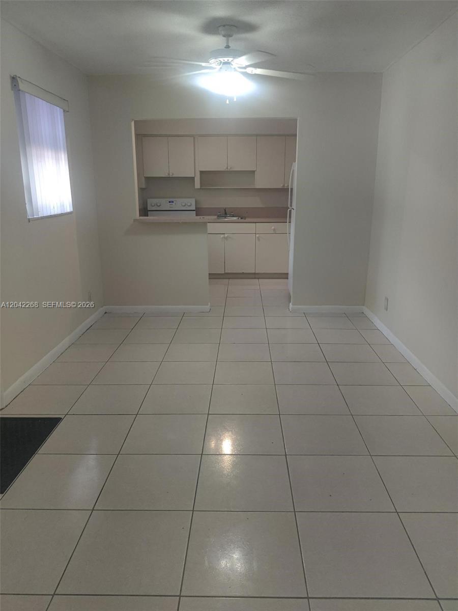 A dining area with light-colored tile flooring leads into a kitchen with white cabinets — 844 SW 10th St # 3, Hallandale Beach FL 33009, HALLANDALE BEACH, FL