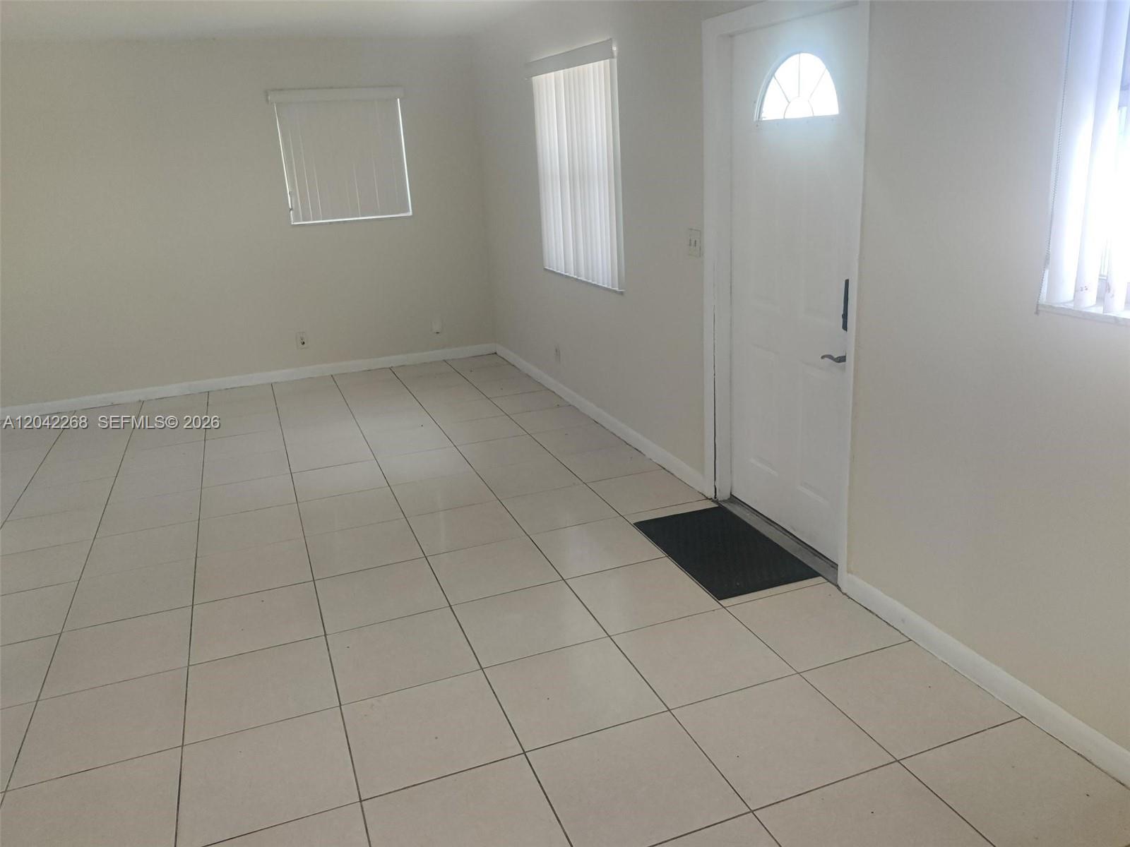 A room with light-colored tile flooring, white walls, vertical blinds, and a white entry door — 844 SW 10th St # 3, Hallandale Beach FL 33009, HALLANDALE BEACH, FL