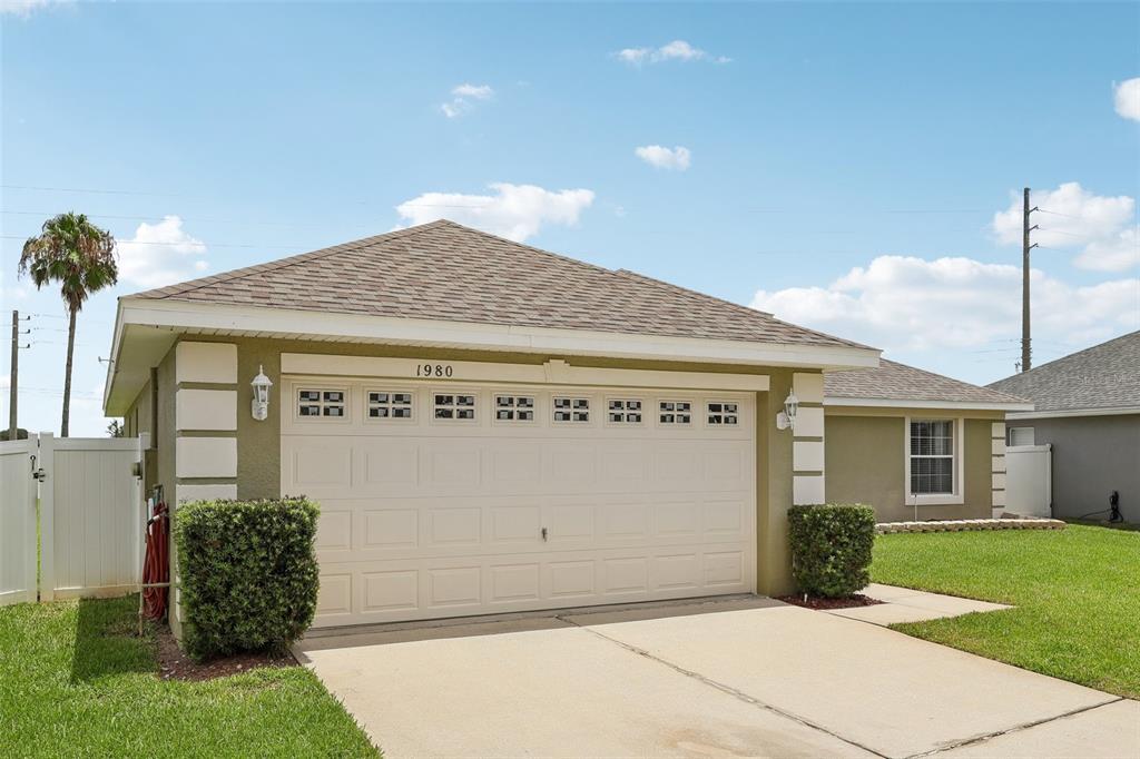 A beige single-story house features a two-car garage, a shingled roof, and a front lawn — 1980 BIG BUCK DRIVE, ST CLOUD, FL