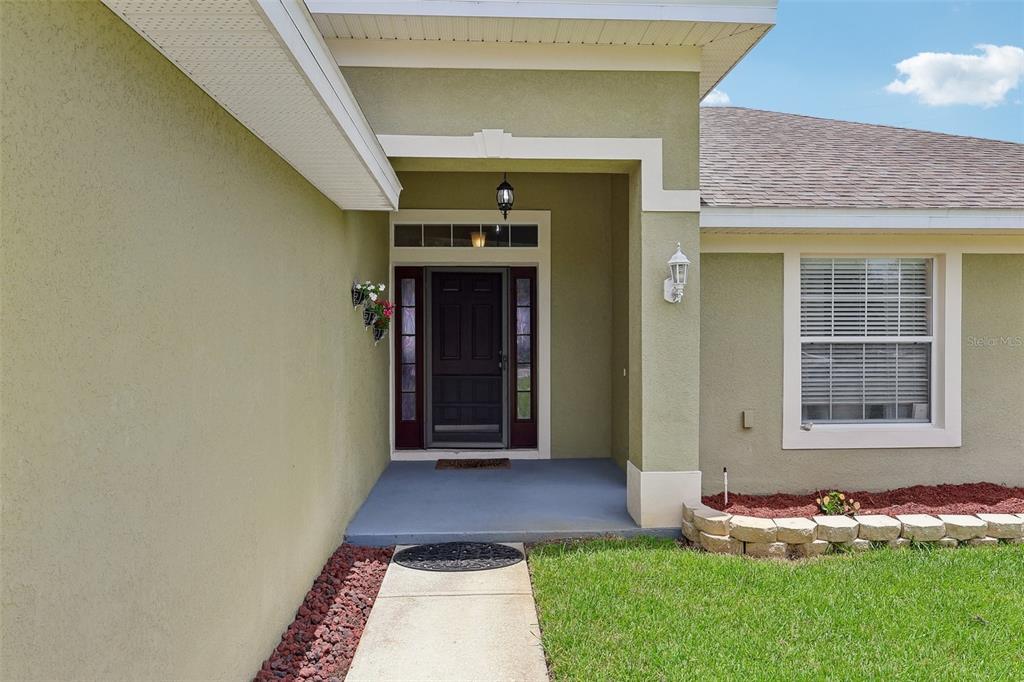 The exterior of a house features a covered entryway with a dark door and walkway — 1980 BIG BUCK DRIVE, ST CLOUD, FL