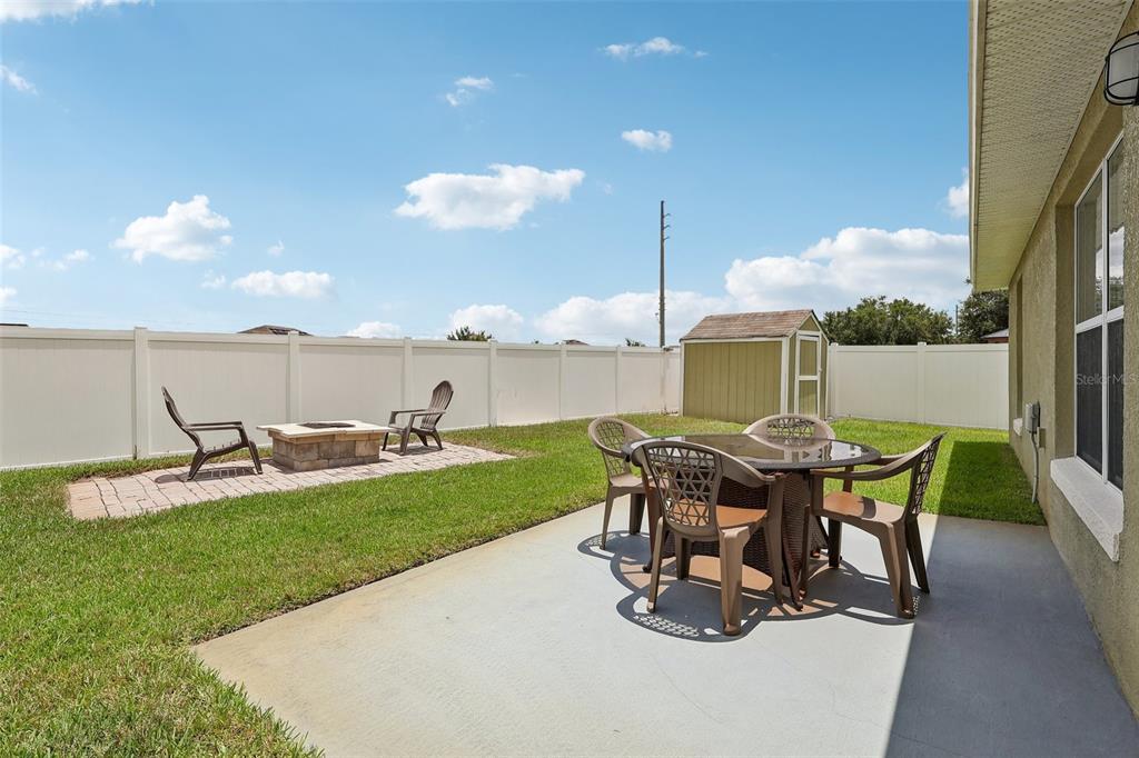 A backyard features a concrete patio with a dining set and a separate paver fire pit — 1980 BIG BUCK DRIVE, ST CLOUD, FL
