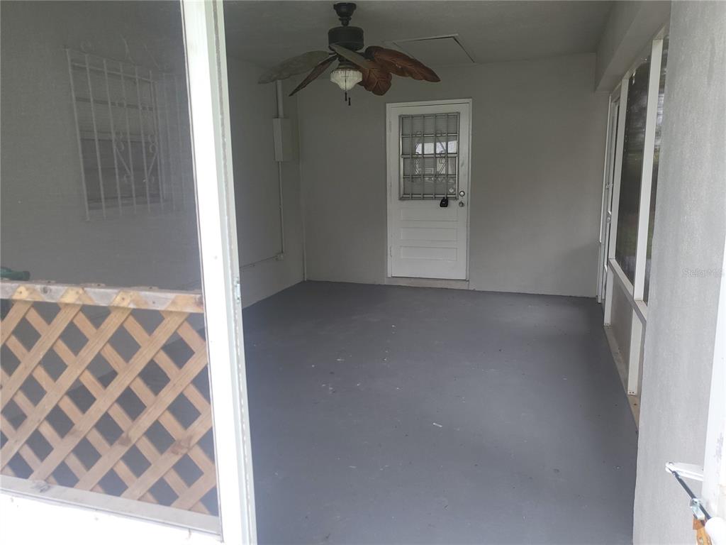 A covered patio features a gray floor, a ceiling fan, and a white door — 2185 NW 3RD STREET, OKEECHOBEE, FL