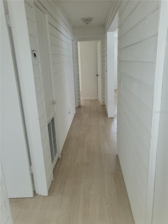 A hallway with white horizontal wood-paneled walls, light wood-look flooring, and multiple doorways — 2185 NW 3RD STREET, OKEECHOBEE, FL