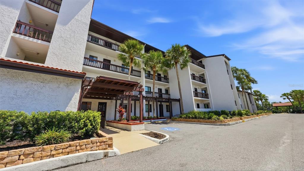 A multi-story white apartment building with a wooden pergola entrance and palm trees — 1602 STICKNEY POINT ROAD UNIT 2-104, SARASOTA, FL