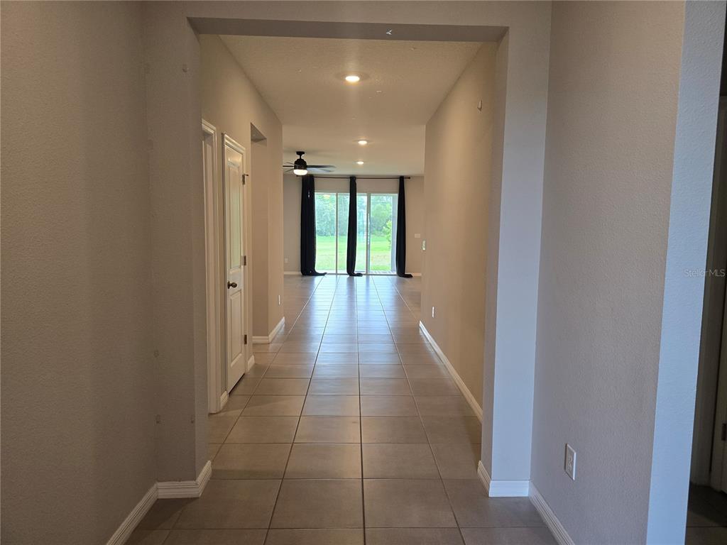 A tiled hallway leads to a living area with sliding glass doors overlooking a yard — 11370 TIMBER GROVE LANE, BROOKSVILLE, FL