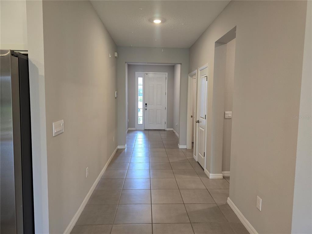 A hallway with light gray walls and tiled flooring leads to a white front door — 11370 TIMBER GROVE LANE, BROOKSVILLE, FL
