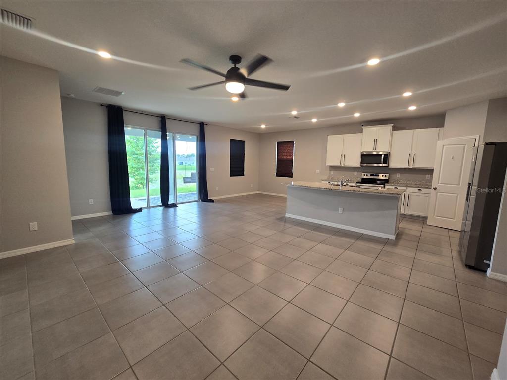 An open-concept kitchen and living area features tile flooring, white cabinetry, and sliding glass doors — 11370 TIMBER GROVE LANE, BROOKSVILLE, FL