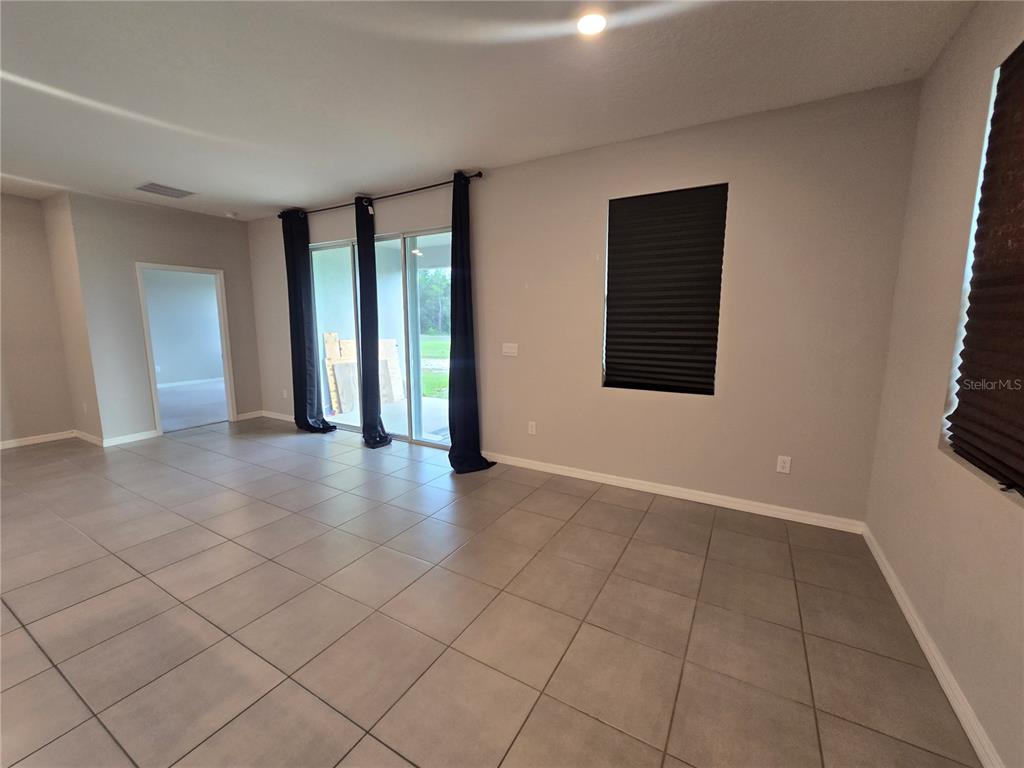 A living room features large gray floor tiles, light gray walls, and sliding glass doors — 11370 TIMBER GROVE LANE, BROOKSVILLE, FL