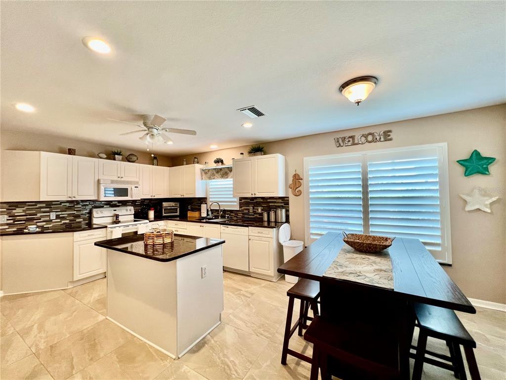 A kitchen features white cabinets, a dark island, tile flooring, and a dining table — 1010 ISLAMORADA BOULEVARD, PUNTA GORDA, FL