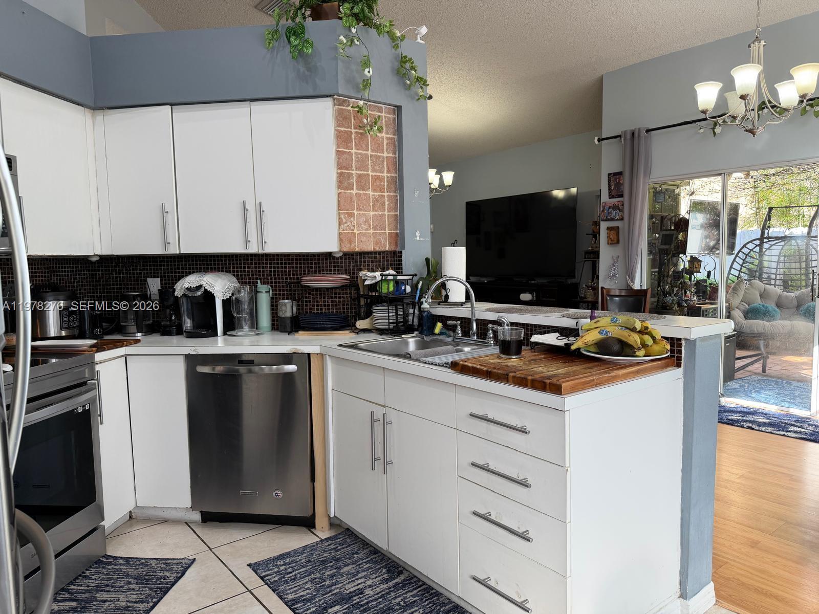 A kitchen features white cabinets, stainless steel appliances, and a peninsula overlooking a living area — 400 Somerset Way, Weston FL 33326, WESTON, FL