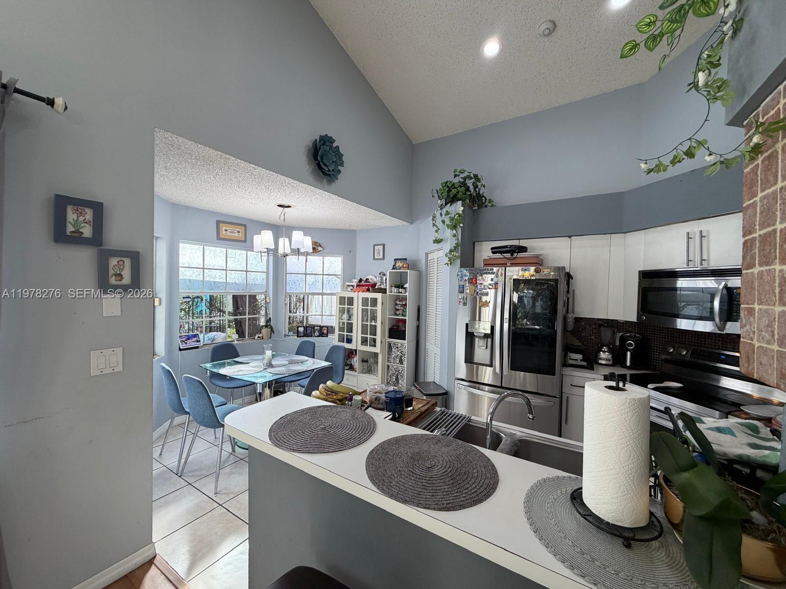 A kitchen with white cabinets and stainless steel appliances overlooks a small dining area — 400 Somerset Way, Weston FL 33326, WESTON, FL