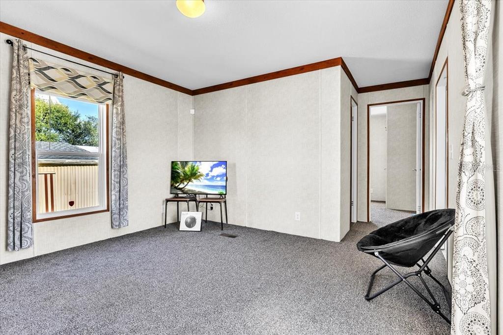 A bedroom with gray carpet, white paneled walls, a window, and a black folding chair — 3702 DUNREATH ROAD, PORT CHARLOTTE, FL