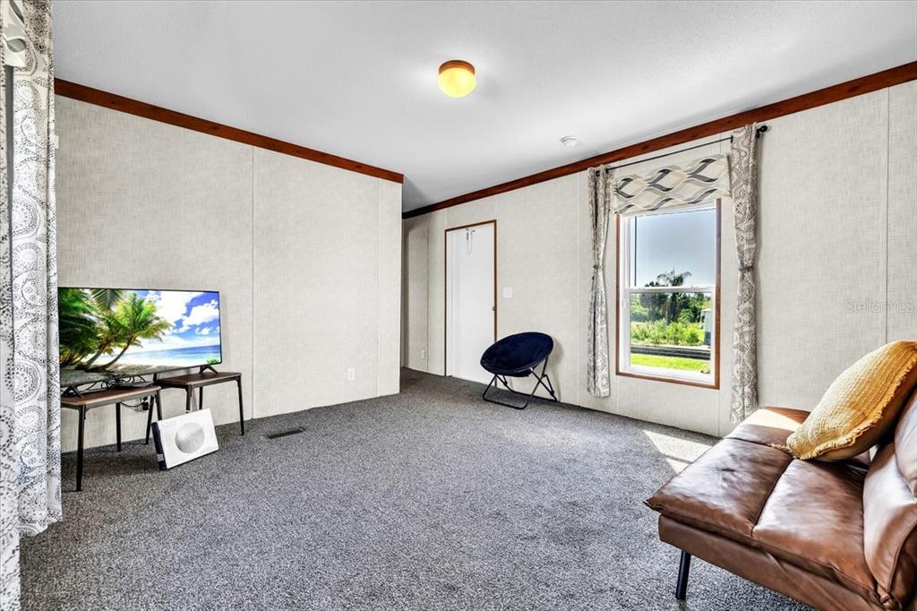 A living room with gray carpet, paneled walls, a television, and a brown leather sofa — 3702 DUNREATH ROAD, PORT CHARLOTTE, FL